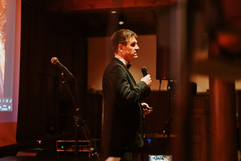 A man in a suit standing on a stage talking to a microphone.