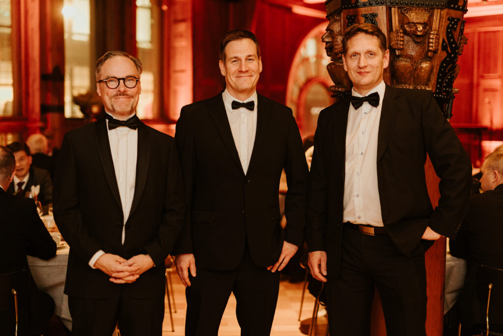 Three men in suits standing in a row and smiling