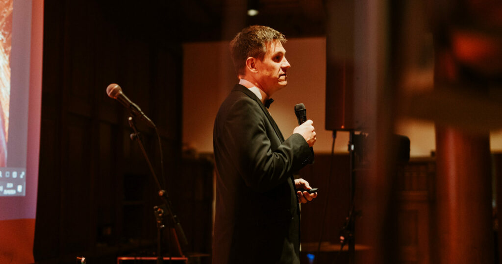 A man in a suit standing on a stage giving a speech